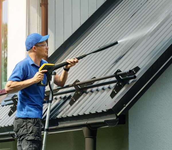 man standing on ladder and cleaning house metal roof with high pressure washer
